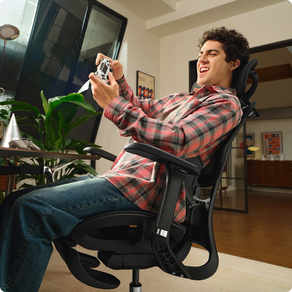 Person sitting in a black e3 air 2026 office chair holding a gaming controller in a room with a desk and computer setup ~scene